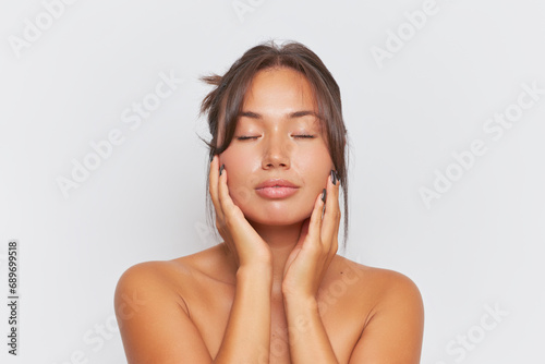 Portrait of beautiful girl with naked shoulders holding hands on her cheeks with closed eyes, skincare product concept, copy space