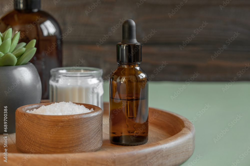 Natural cosmetics advertising scene. Two amber bottles is on a wooden plate with sea bath salt and moisturizer. Blurred wood background. Essential oils. Place for text. SPA massaging concept. Health