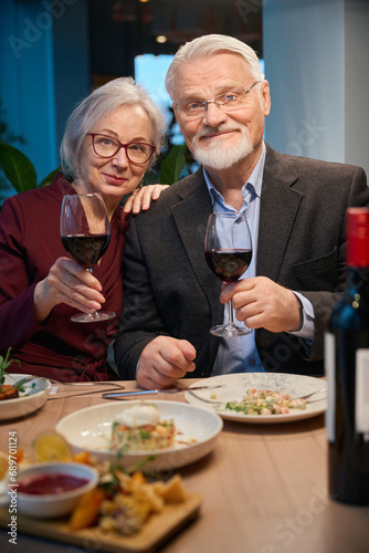 Cheerful senior woman and man holding glasses of wine celebrating New Years Eve