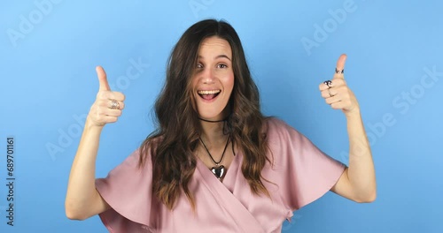 Young woman making good-bad sign isolated on blue background. Girl make choice, or makes a decision thumb up or thumb down, like or dislike, yes or no. Woman change emotions, raised hands, unsure. photo