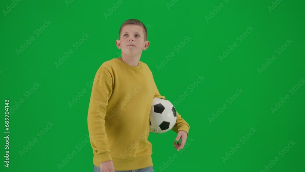 Portrait of boy on chroma key green screen. Schoolboy in casual walking holding football ball and looking around. Profile shot. Portrait of boy on chroma key green screen. Schoolboy in casual walking holding football ball and looking around. Profile shot.