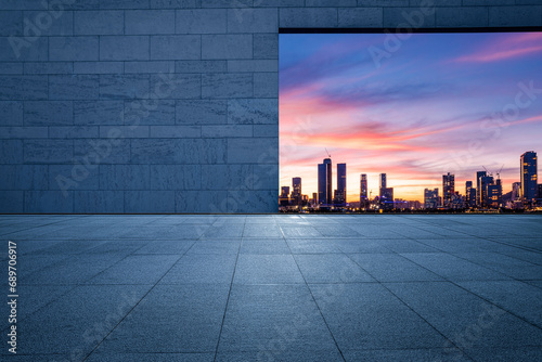 Empty square floor and brick wall with city skyline at sunset