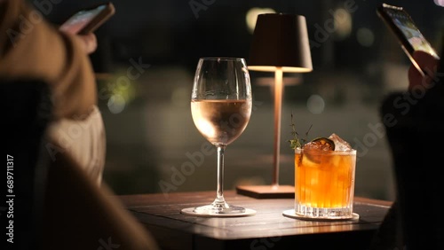 Primo piano su un calice di vino e su un Cocktail illuminati da una lampada da tavolo.
Due persone scattano foto con lo smartphone. photo