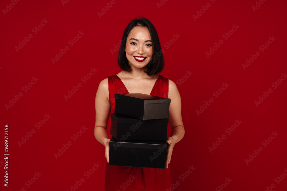 Beautiful asian woman holding gift boxes and smiling at camera isolated over red background Beautiful asian woman holding gift boxes and smiling at camera isolated over red background
