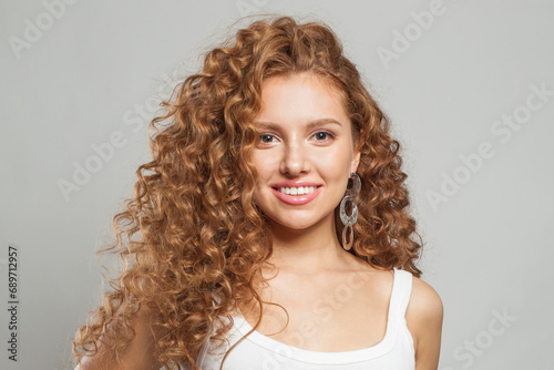 Friendly young female model healthy woman with long wavy frizzy hairstyle and clear skin studio portrait. Hair care, facial treatment and cosmetology concept