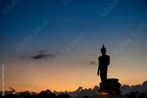 Stand big Buddha Statue in silhouette sun set Light background in park of Thailand temple.Yellow orange light silhouette dark shadow of image Buddha statue stand Buddha tall walk in sun light cloud.