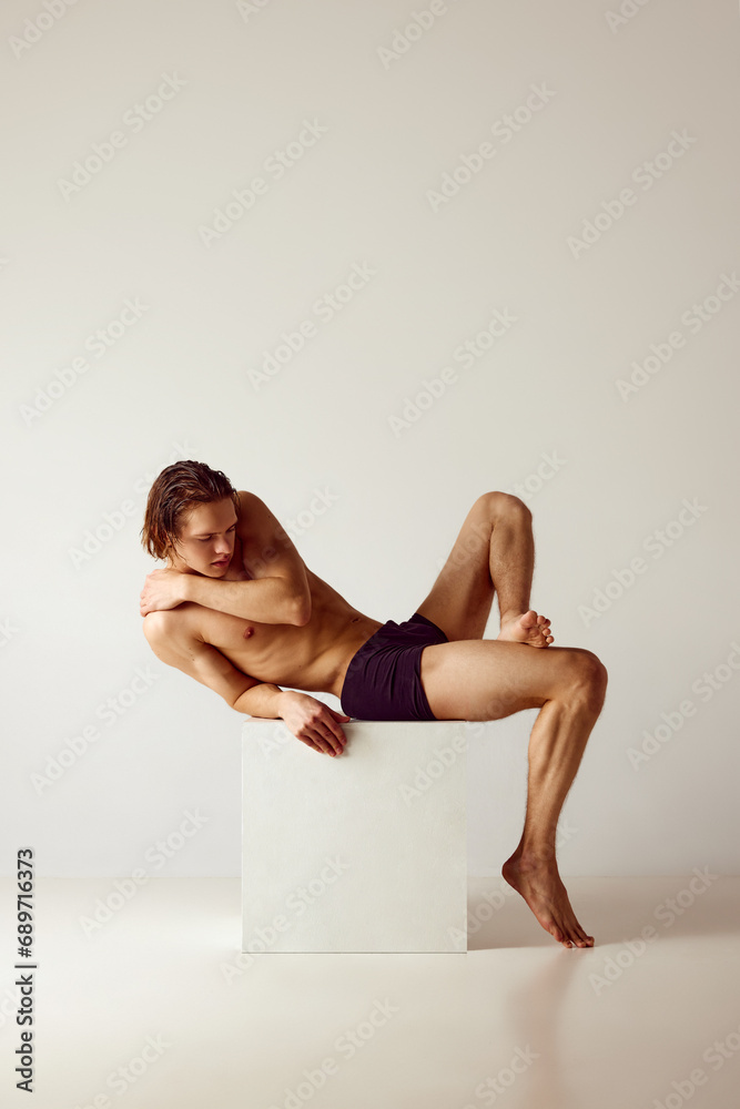 Young shirtless man fir muscular, fit body shape posing shirtless in underwear against grey studio background. Concept of men's beauty, health, body care, sportive lifestyle Young shirtless man fir muscular, fit body shape posing shirtless in underwear against grey studio background. Concept of men's beauty, health, body care, sportive lifestyle
