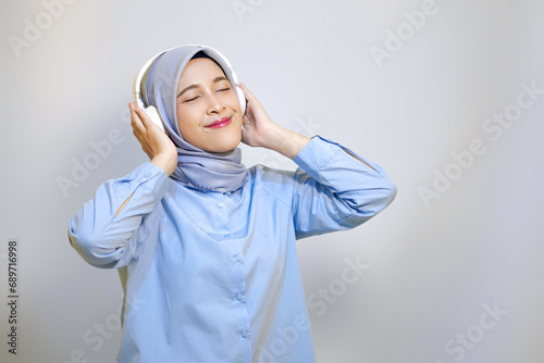 happy young Asian muslim woman listening music with headphone. muslim woman advertising concept. listening music concept © Alfian Muzaki