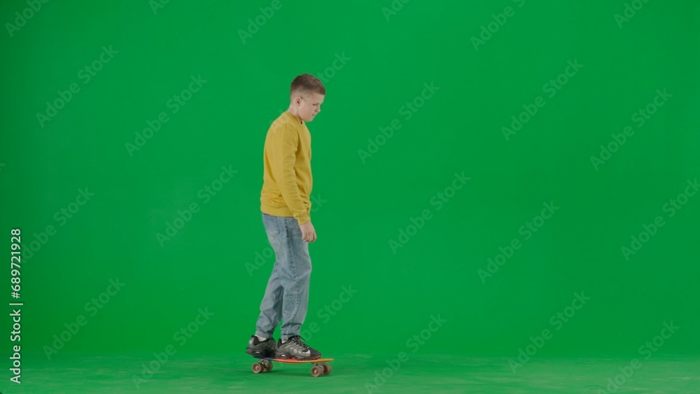 Portrait of kid boy on chroma key green screen. Schoolboy in jeans standing riding on skateboard through the scene, happy face expression. Full body shot Portrait of kid boy on chroma key green screen. Schoolboy in jeans standing riding on skateboard through the scene, happy face expression. Full body shot