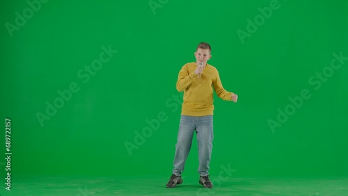 Portrait of kid boy on chroma key green screen. Schoolboy in jeans holding holding karaoke microphone and singing song. Full body front shot.