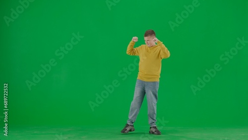Portrait of kid boy on chroma key green screen. Schoolboy in jeans standing with hands up winning gesture positive face expression. Full body front shot. © kinomaster