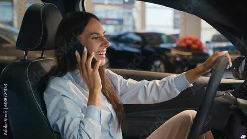 Happy Caucasian successful businesswoman talking mobile phone call friendly conversation joyful woman sit in new car in automobile shop rent service renting buying auto luxury vehicle speak smartphone photo