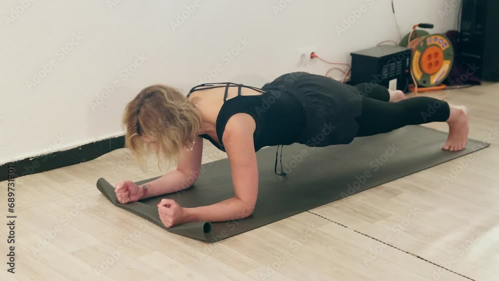 Woman doing plank exercise while practicing yoga. Healthy female is building core muscle stength. She is in black sportswear at gym.