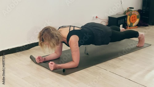 Woman doing plank exercise while practicing yoga. Healthy female is building core muscle stength. She is in black sportswear at gym. photo