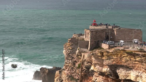 Fort of São Miguel Arcanjo Lighthouse. Situated in Nazaré Portugal. It was first constructed in 1577.  The fort is a popular tourist site. Waves splashing on cliff. Unrecognozable people. photo