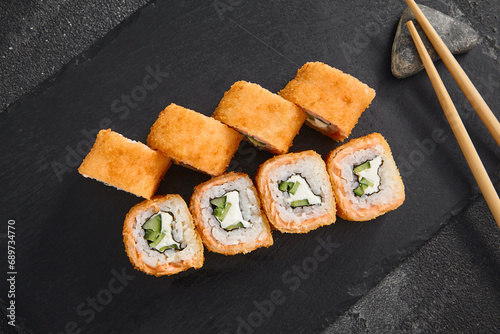 Golden Philadelphia tempura roll filled with salmon, cucumber, and cream cheese, presented on a textured black slate