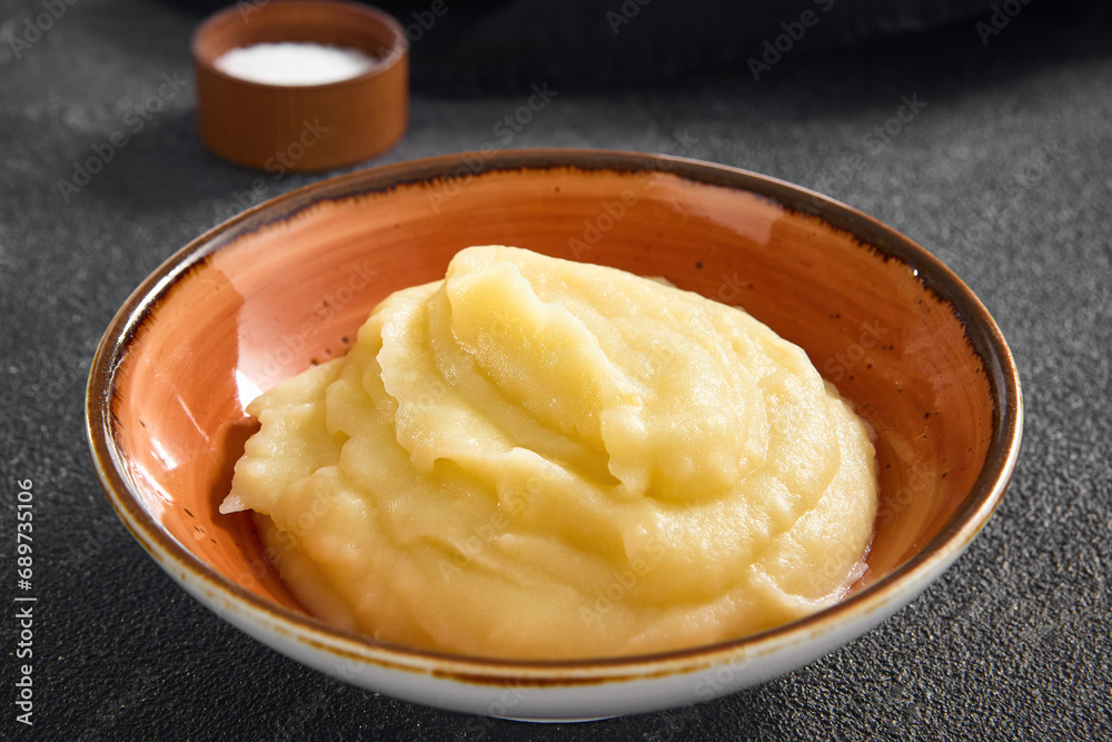 Smooth and buttery mashed potatoes served in a rustic ceramic bowl against a black backdrop, a classic comfort food