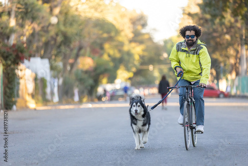 Young Latino man with sunglasses riding a bicycle with his husky dog