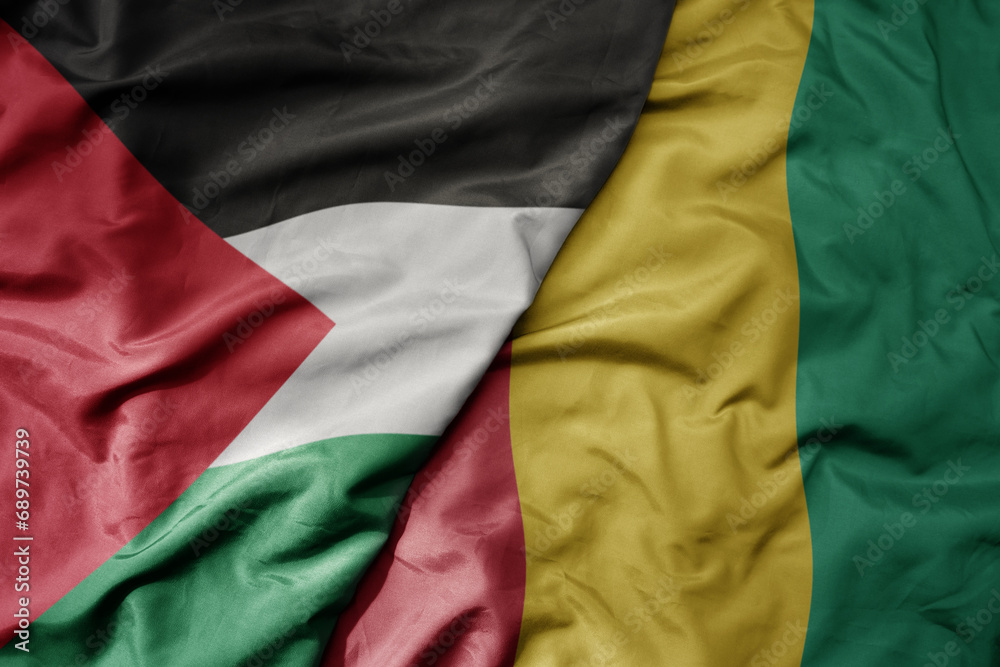 big waving national colorful flag of guinea and national flag of palestine .