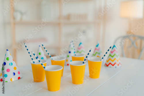 Holiday hats and paper cups with beverage and straws on white table. Festive event. Birthday party celebration concept. Blurred background. Nobody on picture © Natalia
