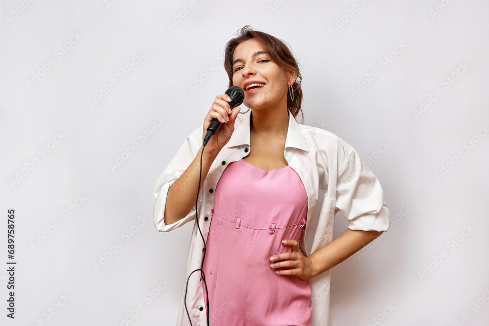 A beautiful cheerful girl in a pink suit and a white shirt sings, holding a microphone in her hand. A beautiful cheerful girl in a pink suit and a white shirt sings, holding a microphone in her hand.