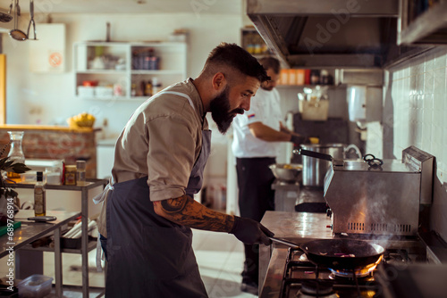 Chef cooking food with fire in pan at restaurant kitchen photo