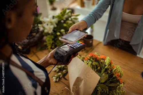 Woman paying bill with smartphone in flower shop