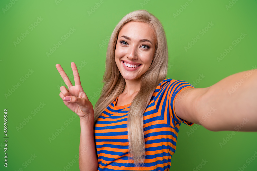 Selfie of attractive young blogger girl greetings with auditory in social media live stream show v sign isolated on green color background Selfie of attractive young blogger girl greetings with auditory in social media live stream show v sign isolated on green color background