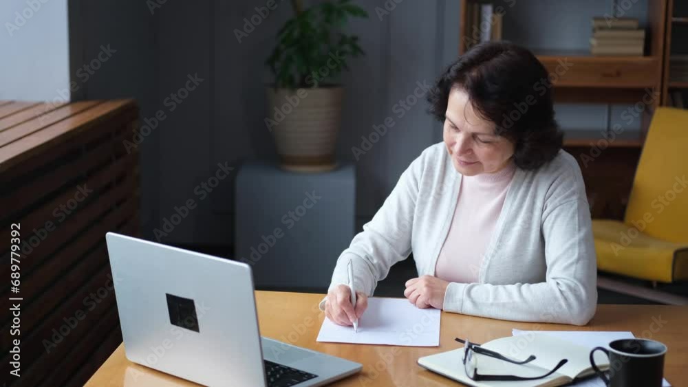 Middle aged senior woman using laptop computer writing notes at home. Focused mature old businesswoman work in home office making written records doing online work. Mature boss professional worker Middle aged senior woman using laptop computer writing notes at home. Focused mature old businesswoman work in home office making written records doing online work. Mature boss professional worker