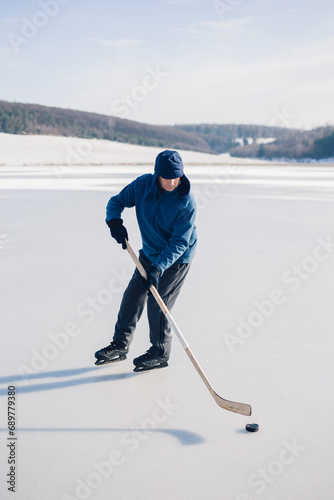 Photography Senior man playing hockey on a frozen lake in winter.