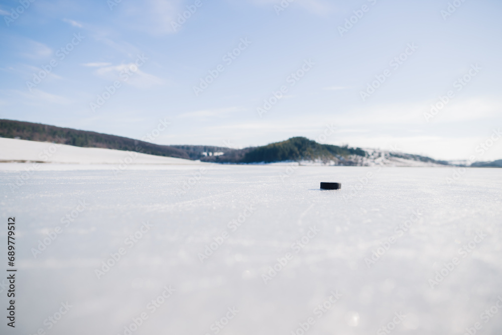 Hockey puck on a frozen lake in winter against the background of mountains.