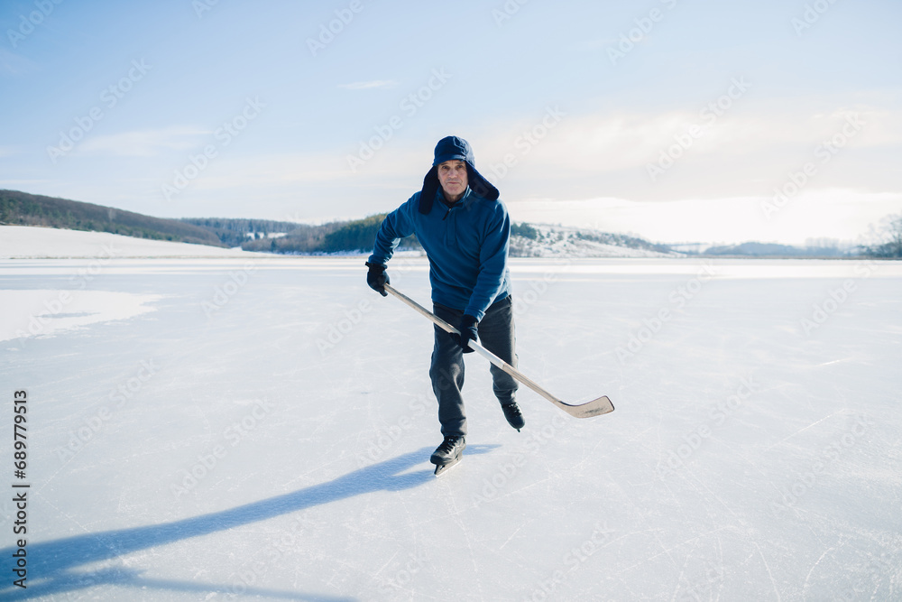 Senior man with hockey stick skating on ice in winter. Looking into the camera. Senior man with hockey stick skating on ice in winter. Looking into the camera.