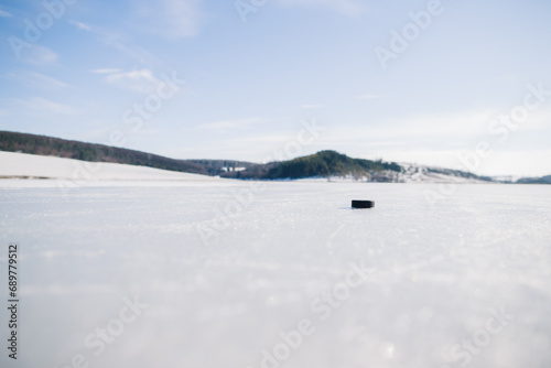 Hockey puck on a frozen lake in winter against the background of mountains. © dsheremeta