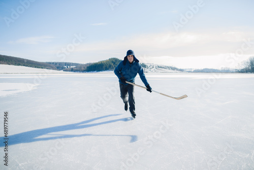 Senior man on ice skates with hockey stick on frozen lake in winter. Hobby concept of elderly people.