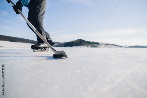 An elderly man practices stricking the puck with hockey stick on a frozen lake in winter.