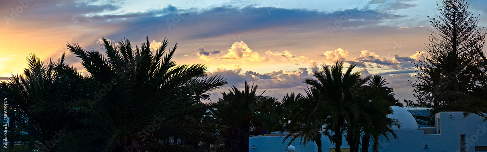 Sunset on the island of Jerba. Beautiful sunset sky over palm trees and houses of Tunisia. Holidays at the resort. Panorama.