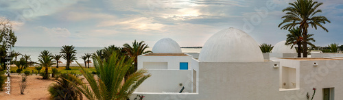 Tunisia. Resort. Palm trees, houses with round arches, against the backdrop of the sea and sky. Coastline. Panorama. photo