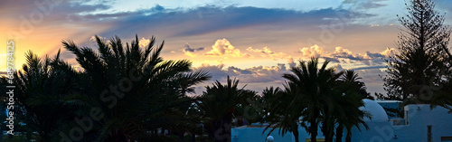 Sunset on the island of Jerba. Beautiful sunset sky over palm trees and houses of Tunisia. Holidays at the resort. Panorama.