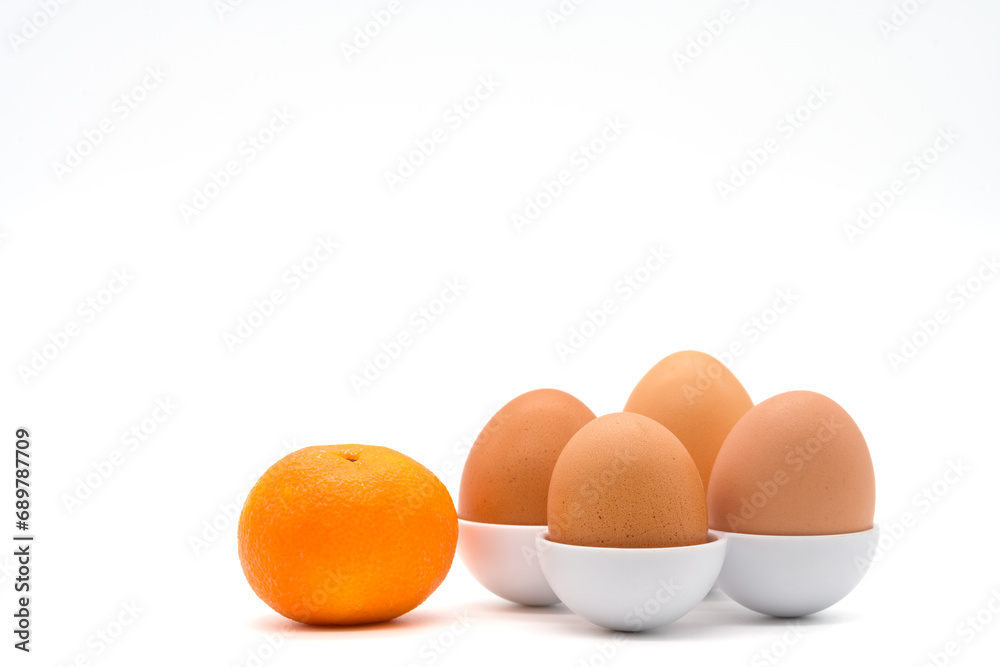 Four chicken eggs in different sizes in egg holders near tangerine isolated on a white background Four chicken eggs in different sizes in egg holders near tangerine isolated on a white background