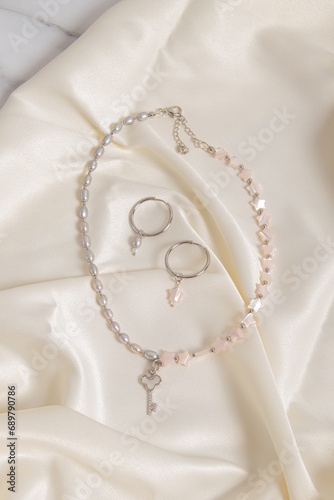 Set of jewelry made of mother of pearl. Necklace and earrings on silk background. Hoop earrings
