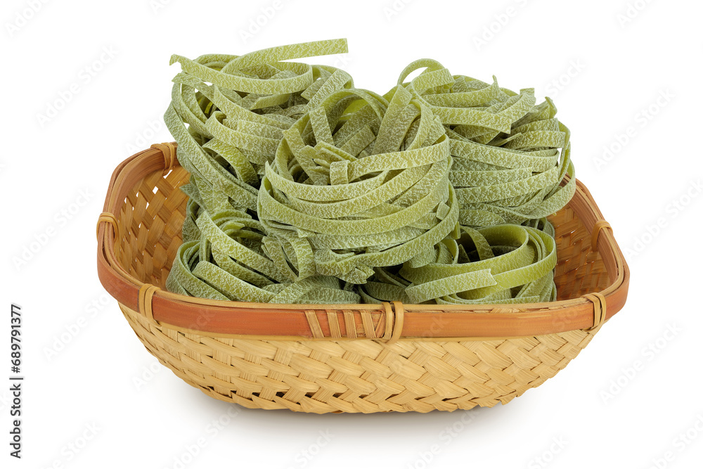 Raw tagliatelle green pasta with spinach in a wicker basket isolated on white background