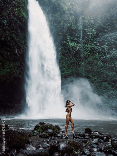 Gorgeous young woman in bikini posing near waterfall in Bali.
