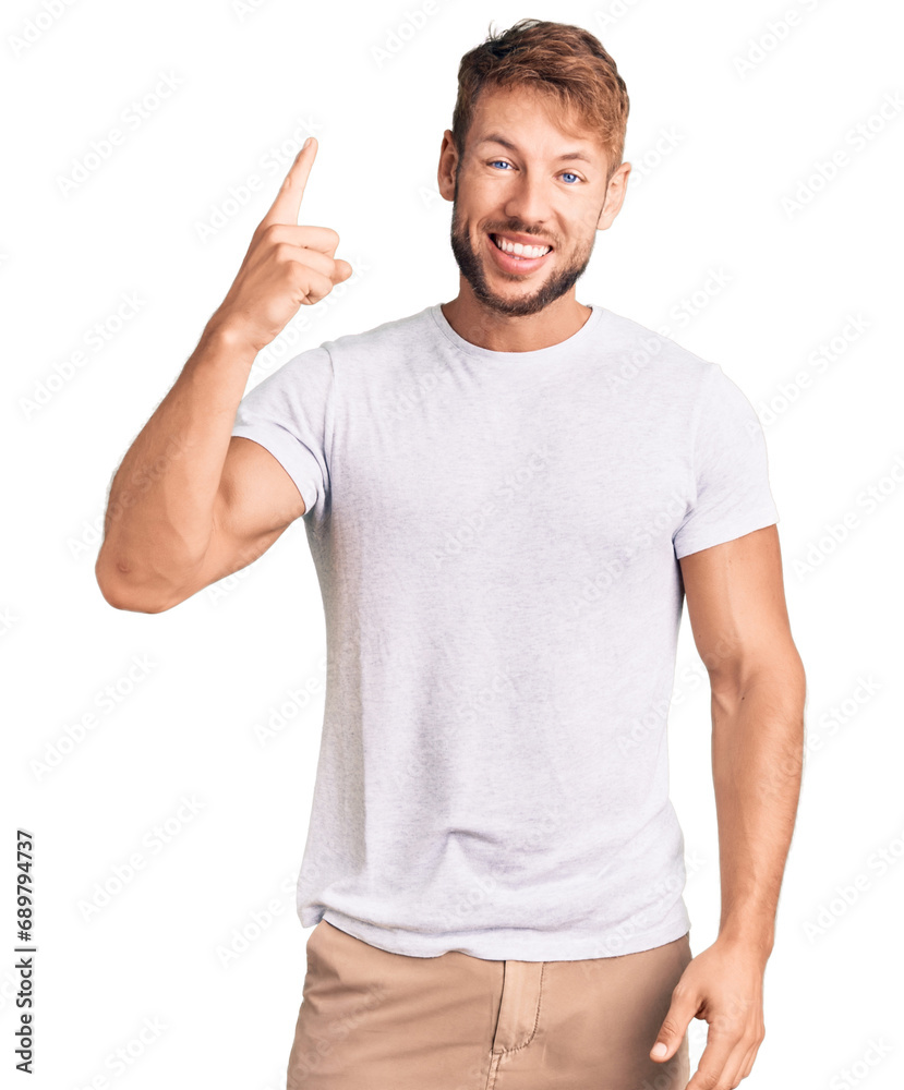Naklejka premium Young caucasian man wearing casual white tshirt pointing finger up with successful idea. exited and happy. number one.