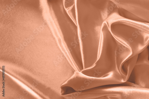 Trendy color peach fuzz smooth silk background. Elegant bright satin with waves. Fabric backdrop. View from above. Luxury cloth texture.