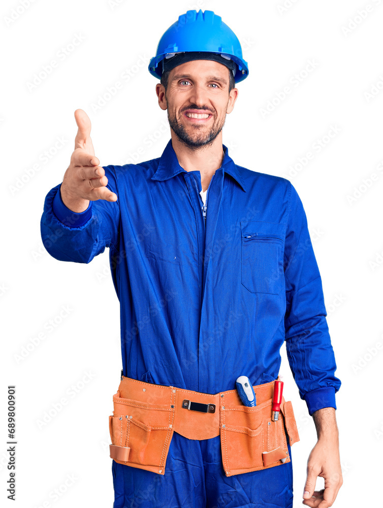 Young handsome man wearing worker uniform and hardhat smiling friendly offering handshake as greeting and welcoming. successful business.