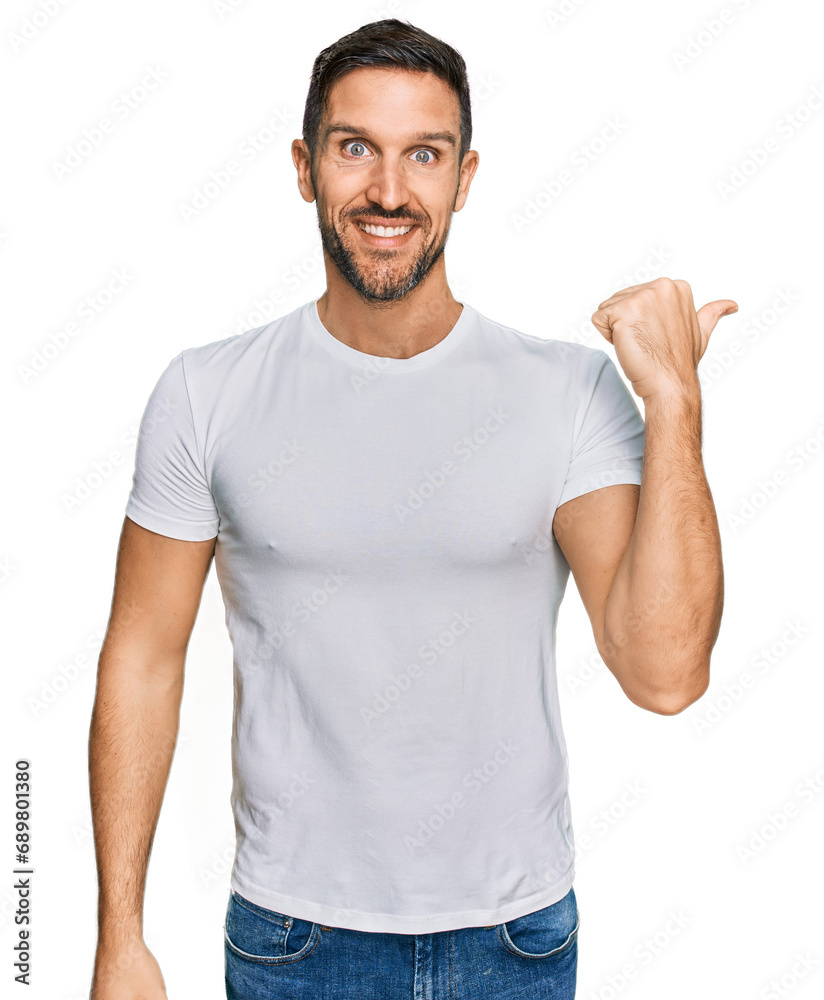 Handsome man with beard wearing casual white t shirt smiling with happy face looking and pointing to the side with thumb up. Handsome man with beard wearing casual white t shirt smiling with happy face looking and pointing to the side with thumb up.