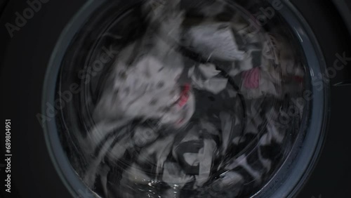 Close-up of spinning drum with dirty laundry of washing machine at home. Household chore and housework concept photo
