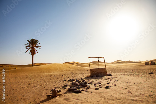 Old water well in the desert with palm tree and dunes in the background photo