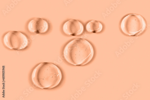 Cosmetic hydrating product or ingredient concept. Peach fuzz color drops of transparent liquid on a trendy color background. Drops gel or oil close up.