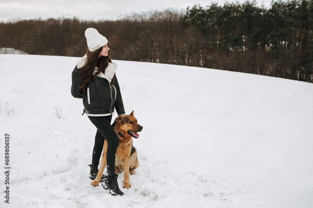 Young woman walk the dog German Shepherd in winter field forest, running playing with snow, training the animal in harsh conditions, wind blowing. Christmas Time, New Year

